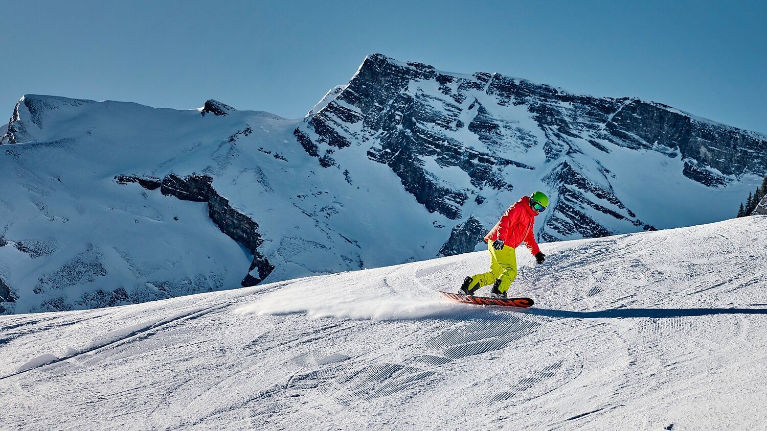 Ein Snowboardfahrer fährt auf der Piste auf der Stockhütte, im Hintergrund das Bergpanorama