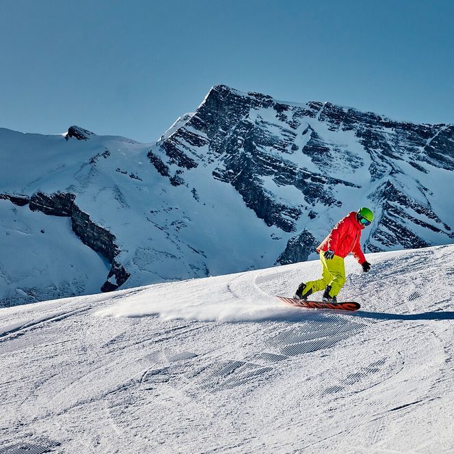 Ein Snowboardfahrer fährt auf der Piste auf der Stockhütte, im Hintergrund das Bergpanorama
