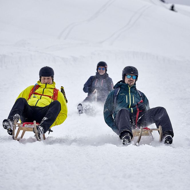 Die dreiköpfige Männergruppe erlebt eine rasante Abfahrt auf der Schlittelpiste Klewenalp-Stockhütte.